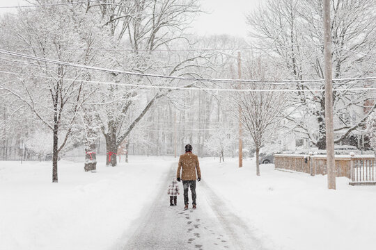 Father And Toddler Son Walk Down An Icy Street On A Snowy Day