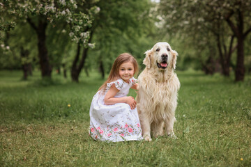little girl in a dress and a straw hat hugs a golden retriever labrador dog