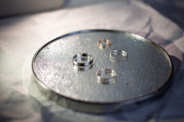 Wedding rings of the newlyweds with white gold lie on the mirror