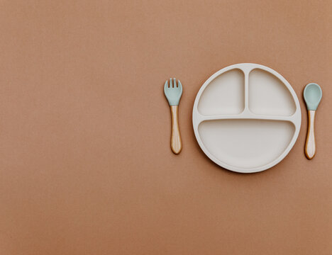 Composition with baby food accessory. Silicone plate on brown background. Neutral pastel colors