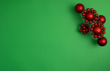 Red Christmas baubles decoration on green background with copy space. New Year greeting card. Minimal style. Flat lay.