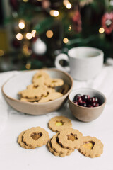 DIY Stained Glass Christmas Cookies on white table with mug and cranberries bowl, in cozy home with bokeh background. Fun and creative cooking project. Home backing lifestyle. 