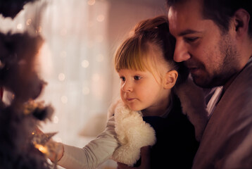 Merry Christmas and Happy Holidays! Dad and daughter decorate the Christmas tree indoors. The morning before Xmas. Portrait loving family close up. - 475603549