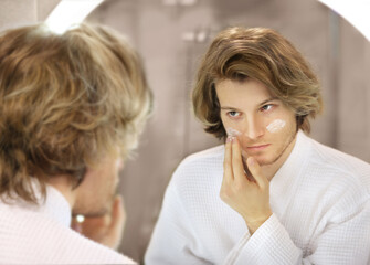 Fototapeta premium young man looking in the mirror,combing his hair,looking at problems on face