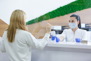 Shot of a female person being measured body temperature with a contactless thermometer by the employee of the reception desk of a modern hospital. Compliance with measures for the non proliferation of