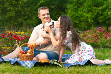 Happy family, young couple in the garden at a picnic. Enamored woman and man on the grass with their dog jack russell terrier