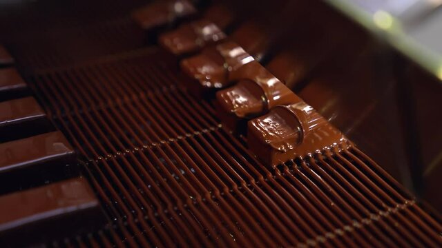 Bars of sweets covered with chocolate. Chocolate bars move along conveyor belt at confectionery factory for the production of sweets. Close up.