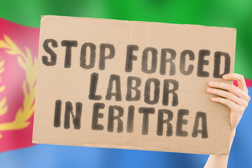 The phrase " Stop forced labor.in Eritrea " on a banner in men's hand with blurred Eritrean flag on the background. Illegal. Horrible. Stressful. Dangerous. Community. Worker. Violence. Right. Victim