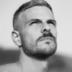 Grayscale portrait of an adult Spanish man with a septum piercing outdoors