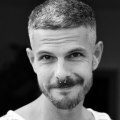 Grayscale portrait of an adult Spanish man with a septum piercing outdoors