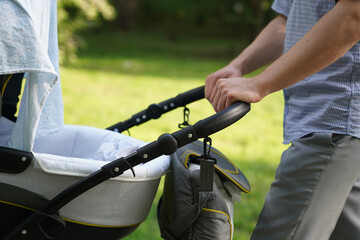 Close-up of men's hands with a stroller, a young dad walking in the park with a baby in a stroller, fatherhood, dad, father's day concept. High quality photo