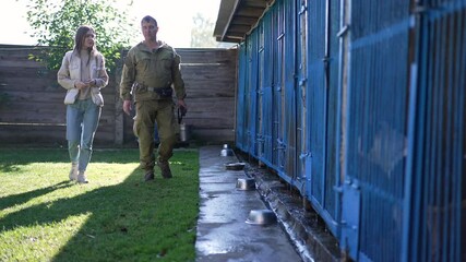 Wide shot young Caucasian woman and adult man talking walking in sunshine outdoors in dog shelter. Beautiful lady choosing pet discussing adoption with professional cynologist trainer