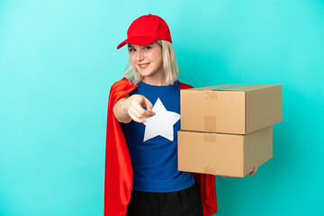 Super Hero caucasian delivery woman isolated on blue background pointing front with happy expression