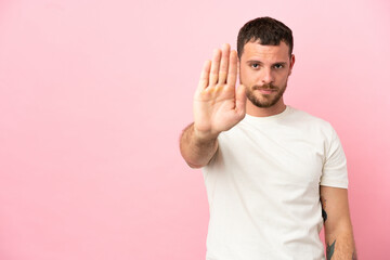Young Brazilian man isolated on pink background making stop gesture
