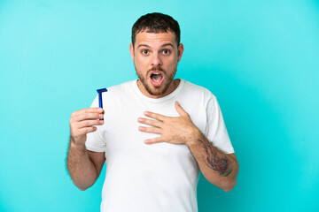 Brazilian man shaving his beard isolated on blue background surprised and shocked while looking right