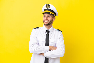 Airplane caucasian pilot isolated on yellow background looking up while smiling