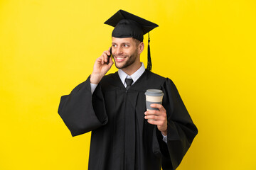Young university graduate caucasian man isolated on yellow background holding coffee to take away and a mobile