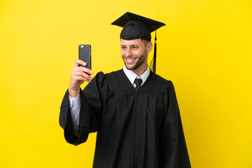 Young university graduate caucasian man isolated on yellow background making a selfie