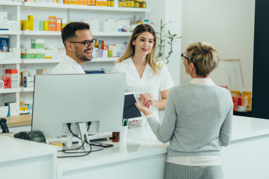 Two pharmacist giving prescription medications to senior female customer in a pharmacy