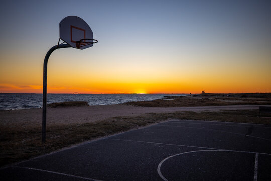 Empty outdoor basketball court by a beach with a magnificent colorful sunset in the background