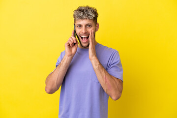 Young caucasian man using mobile phone isolated on yellow background with surprise and shocked facial expression