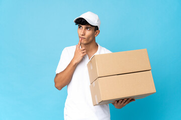 Delivery Argentinian man isolated on blue background having doubts while looking up