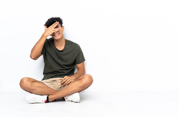 Young Argentinian man sitting on the floor covering eyes by hands and smiling