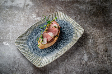 Open bacon and radish sandwich on a gray stone table
