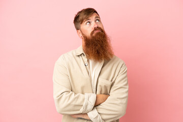 Young reddish caucasian man isolated on pink background and looking up