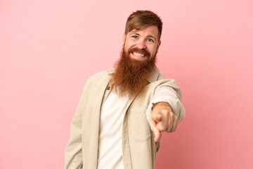 Young reddish caucasian man isolated on pink background pointing front with happy expression