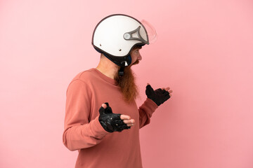 Young reddish caucasian man with a motorcycle helmet isolated on pink background with surprise...