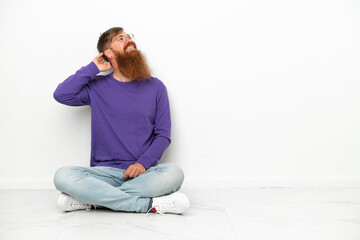 Fototapeta premium Young caucasian reddish man sitting on the floor isolated on white background thinking an idea