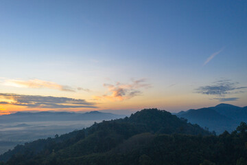 aerial view scenery sunrise above the mountain in tropical rainforest..slow floating fog blowing cover on the mountain look like as a sea of mist. .beautiful sunrise in the mist background.