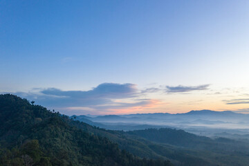 Naklejka premium aerial view scenery sunrise above the mountain in tropical rainforest..slow floating fog blowing cover on the mountain look like as a sea of mist. .beautiful sunrise in the mist background.