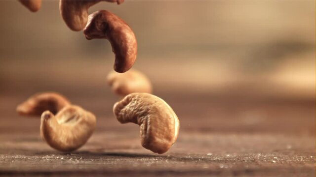 Cashews fall on the table. On a wooden background. Filmed is slow motion 1000 fps. High quality FullHD footage
