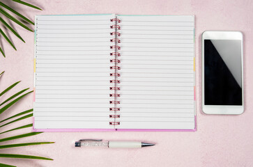 Top view of  empty black notebook, pen and phone on pink background