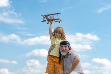 Child boy and grandfather with toy jetpack plane against sky. Child pilot aviator with plane dreams of traveling.