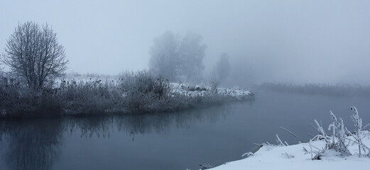 Winter morning in a haze. Trees on river banks in silvery hoarfrost. Magic natural picture.