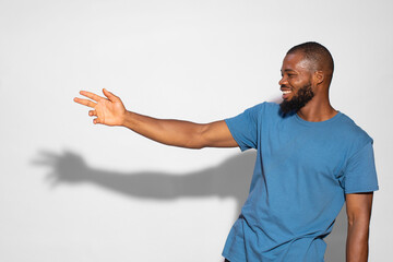 Black man with a blue t-shirt smiling and showing something on a white background. © Nzewi Confidence/Wirestock