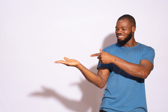 Black man with a blue t-shirt smiling and holding a copy space with hand and showing it.