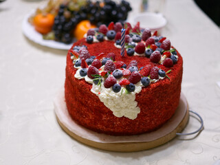 The birthday cake is on the table. Decorated with strawberries and blueberries. There is also a white cream on top