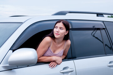A girl with long hair leaned out of the cab of a car on the road, the concept of auto travel