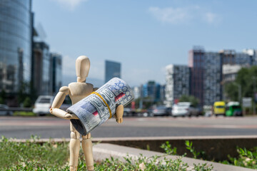 A wooden man holds rolled-up 20,000 Kazakhstani tenge bills against the backdrop of a city street