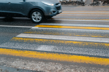 Side view of car at dangerous fast speed crossing pedestrian crosswalk, outdoors in winter. Blurred motion, selective focus on yellow and white stripes on asphalt