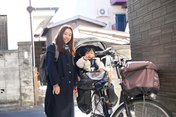 Fototapeta na wymiar 自転車のチャイルドシートに乗る小さい子供と送り迎えをする母親