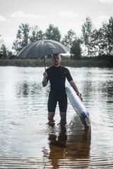 a surfer with an umbrella stands in the water, the concept of bad weather