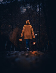 Vertical shot of a young man in a yellow hoodie with a lantern and a leaf walking in the dark forest