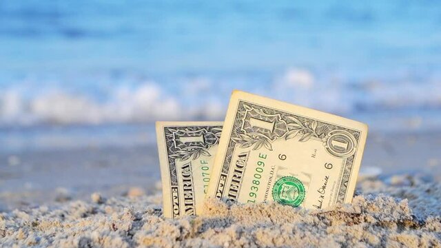 Two one dollar bills half buried in sand on sandy seashore close-up. Two paper dollar bills half in sand on sea beach on sunny day. Concept money, finance, investment, wealth, poverty, financing, cash