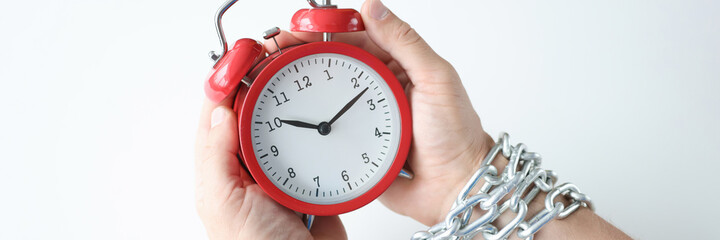 Male hands holding red alarm clock with hands tied by chain closeup