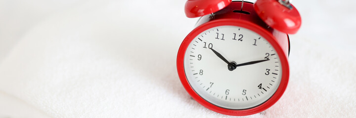 Red alarm clock stands on white towel closeup